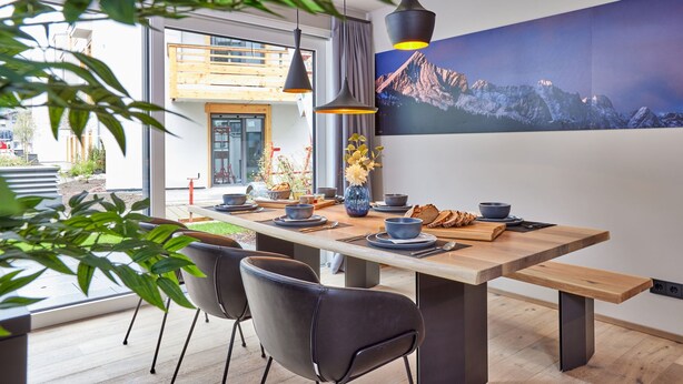 Un espace repas moderne avec une table en bois, des chaises noires et un grand tableau représentant une montagne accroché au mur.