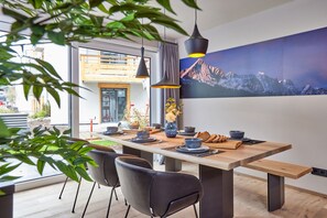 Ein moderner Essbereich mit einem Holztisch, schwarzen Stühlen und einem großen Gemälde von Bergen an der Wand.