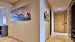 Un couloir doté d’un plancher en bois, d’une porte en bois et de deux tableaux encadrés représentant des montagnes.