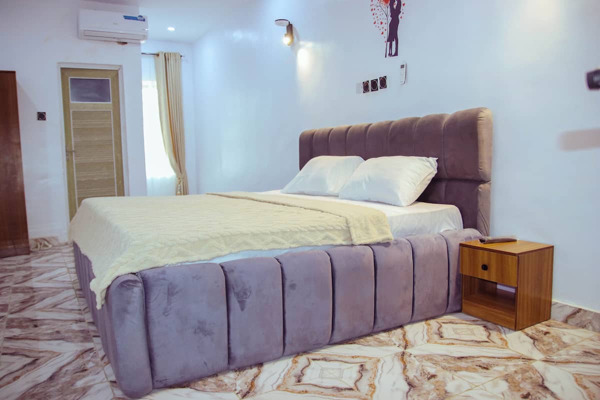 A bedroom with a bed, a nightstand, an air conditioner, and a wall-mounted light fixture.
