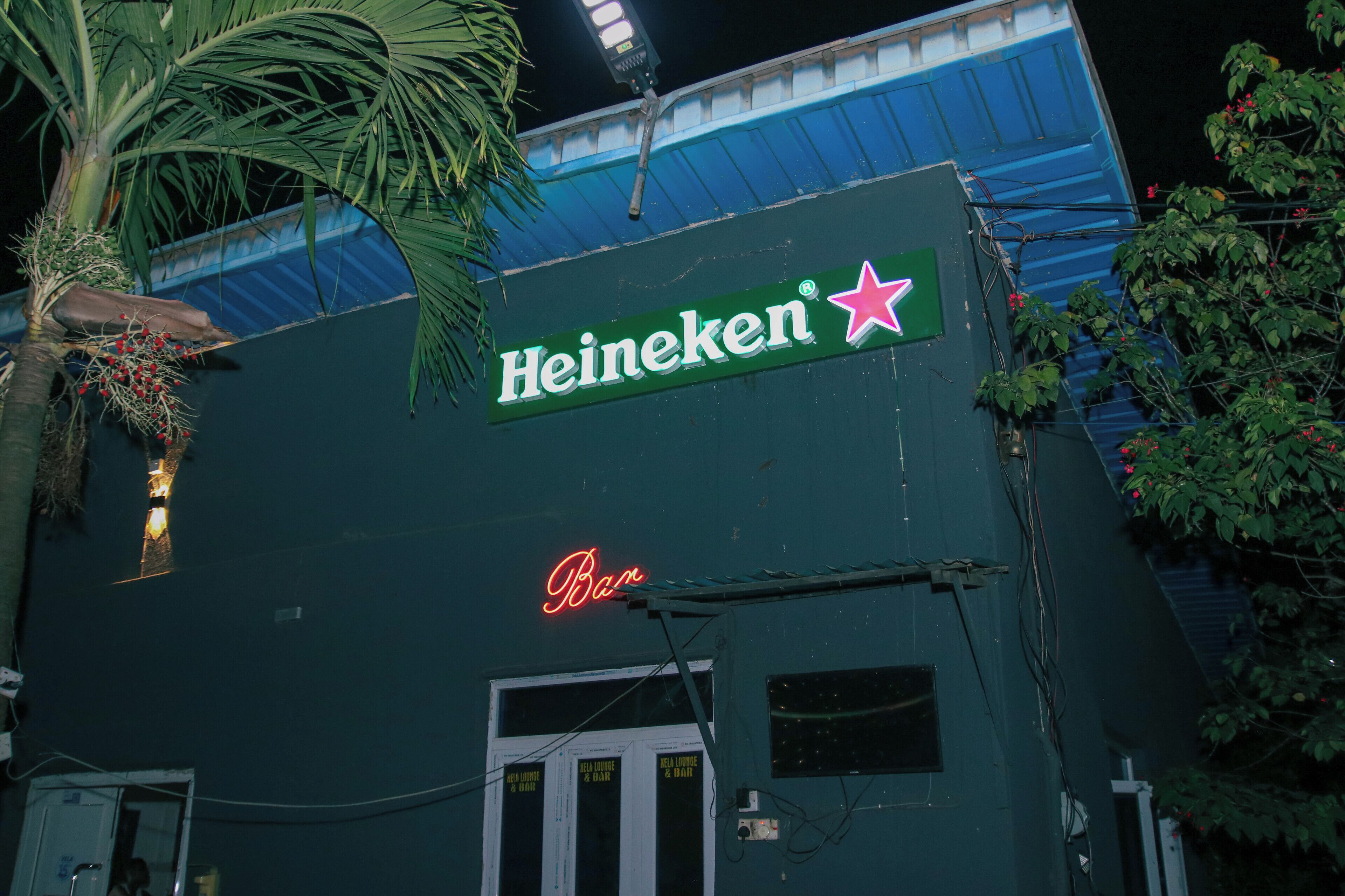 A building with a Heineken sign and a neon bar sign.