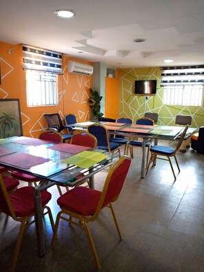 Un salón de conferencias con varias mesas y sillas, unidades de aire acondicionado y una televisión en la pared.