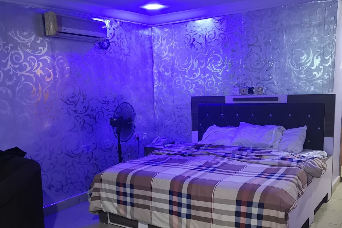 A bedroom with a bed, a fan, and a wall-mounted air conditioner.