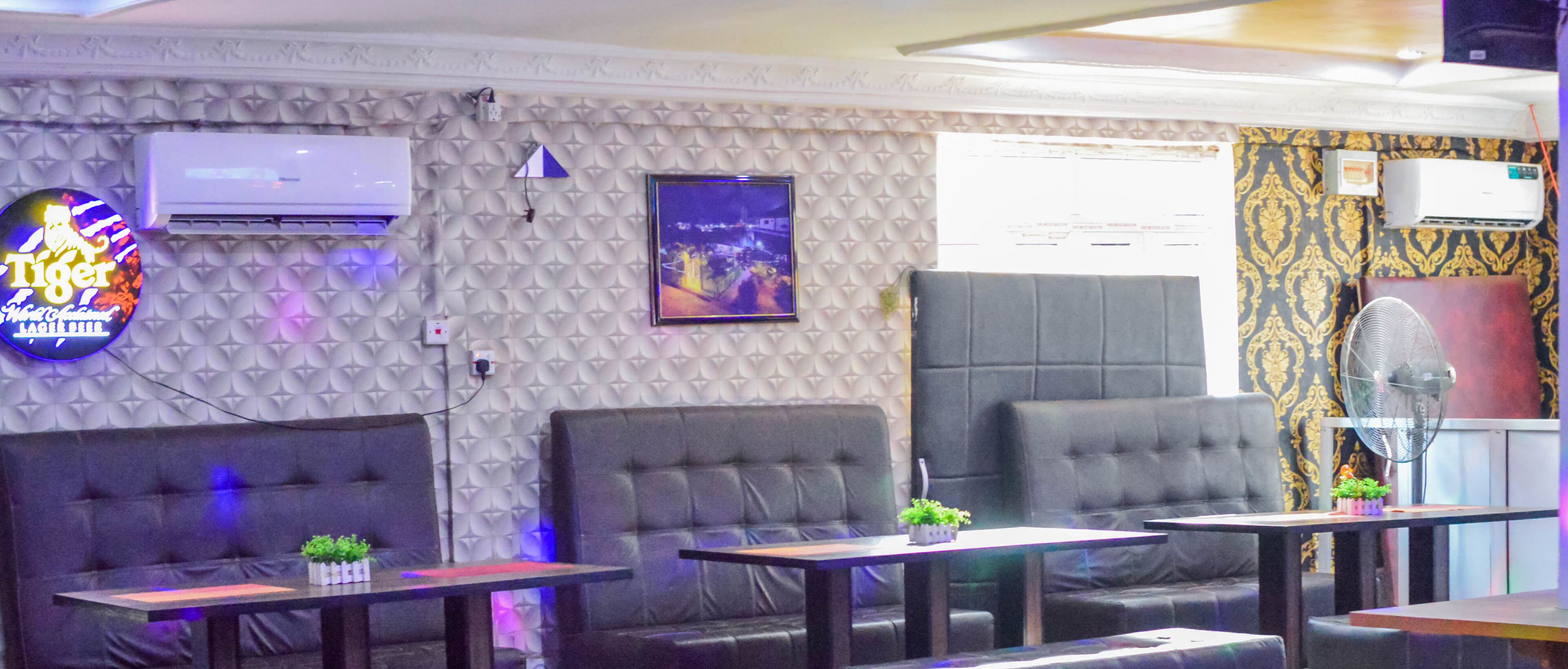 A room with a patterned wall, a flat-screen TV, air conditioning units, and seating with tables.