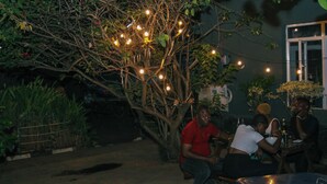 An outdoor seating area with tables and chairs, surrounded by greenery and a tree with string lights. - Xela Hotels and Resorts (Ife)