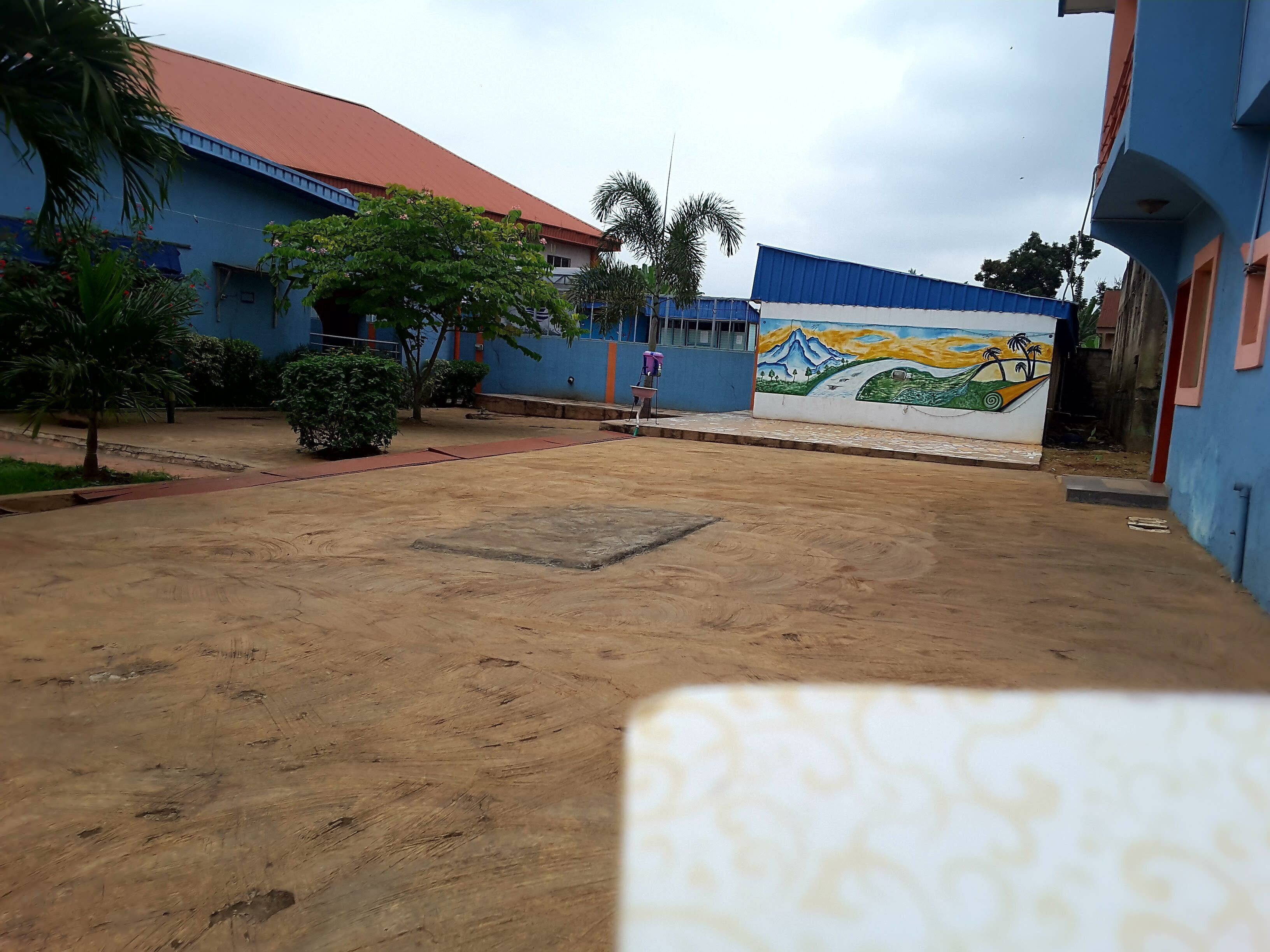 A courtyard with a sandy ground, a mural on the wall, and buildings with blue and red roofs.