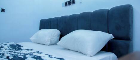 Una cama con cabecera oscura, almohadas blancas y una colcha estampada.