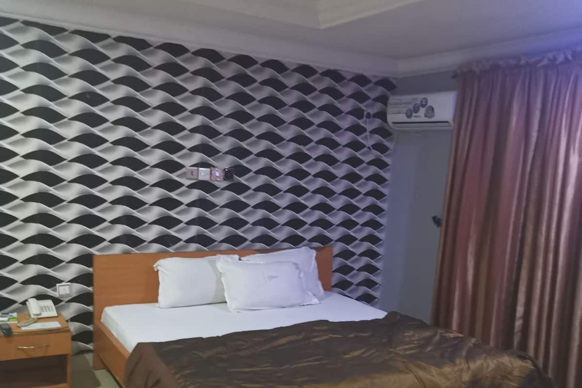 A hotel room with a bed, a nightstand, a telephone, and an air conditioning unit.