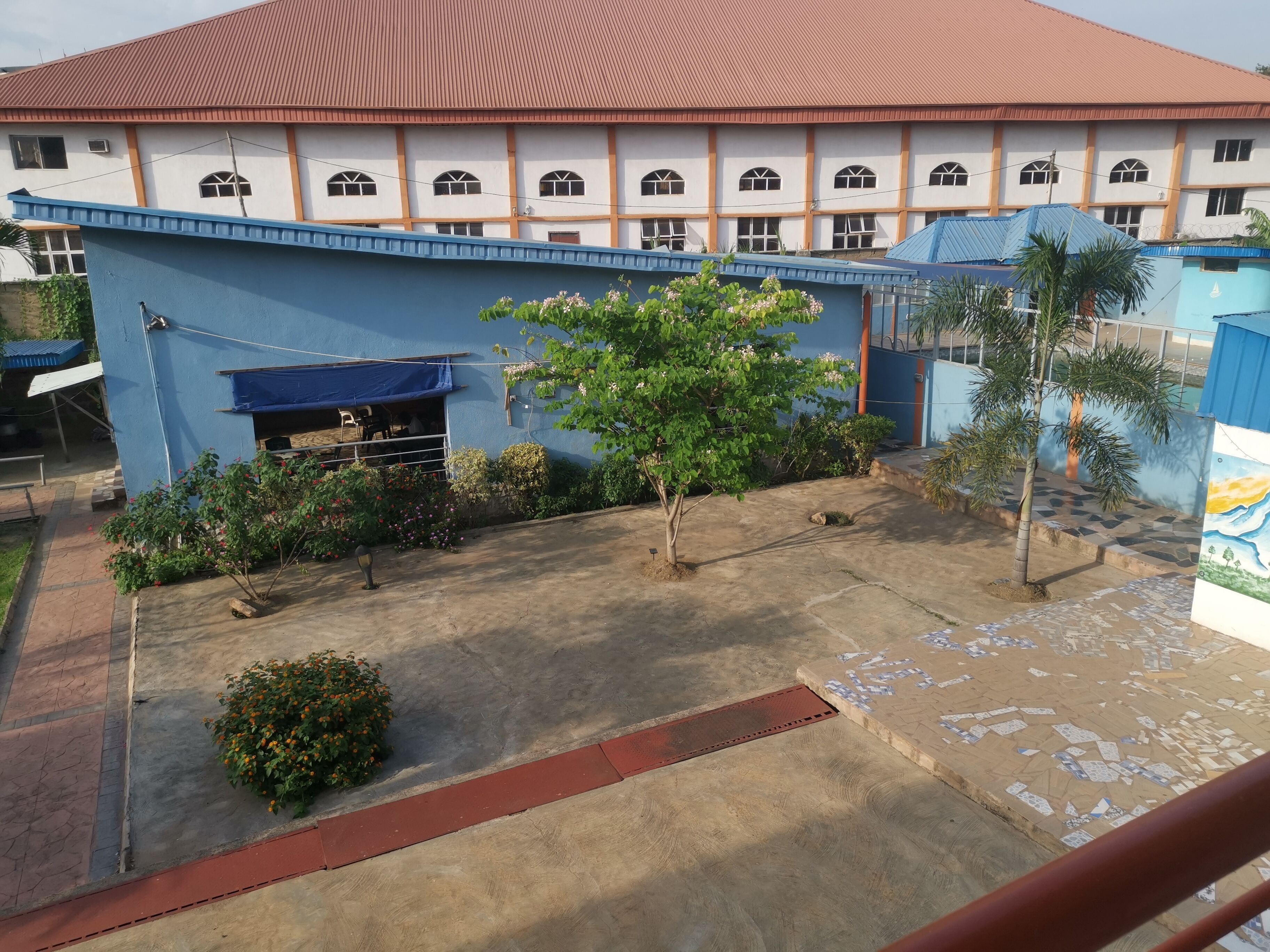A building with a red roof and multiple windows, surrounded by a blue wall and some greenery.