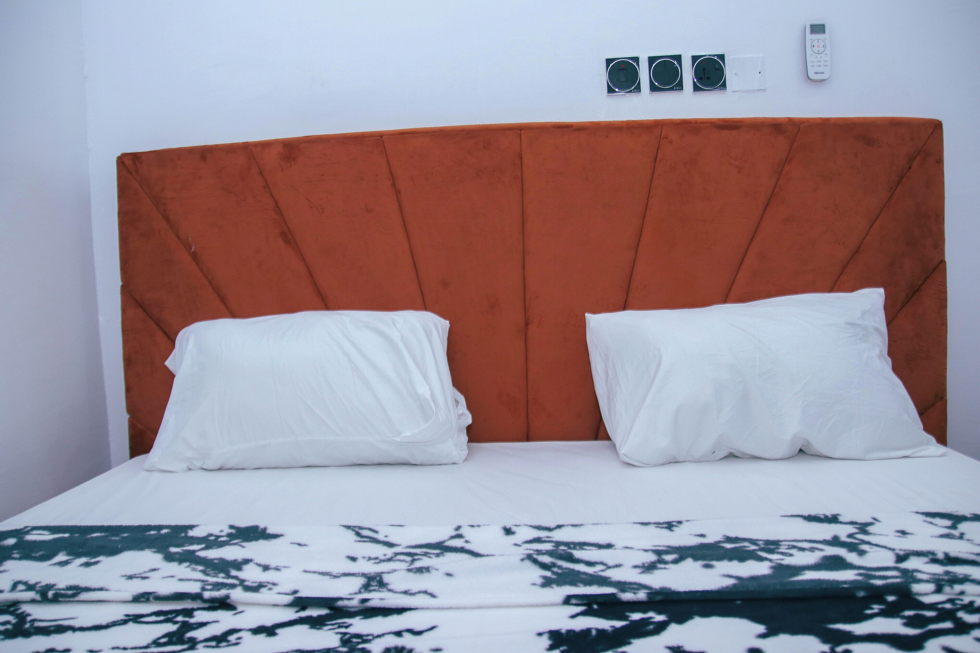 A bed with an orange headboard, white pillows, and a patterned bedspread.