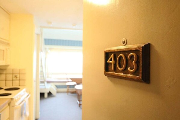 A hallway with a number plate '403' on the wall, leading to a kitchen area with white cabinets and a stove. - Affordable Loft Unit at Inns of Waterville Valley (Waterville Valley)