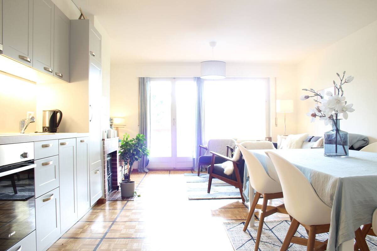 A modern kitchen with white cabinets, a dining area with a table and chairs, and a large window providing natural light.