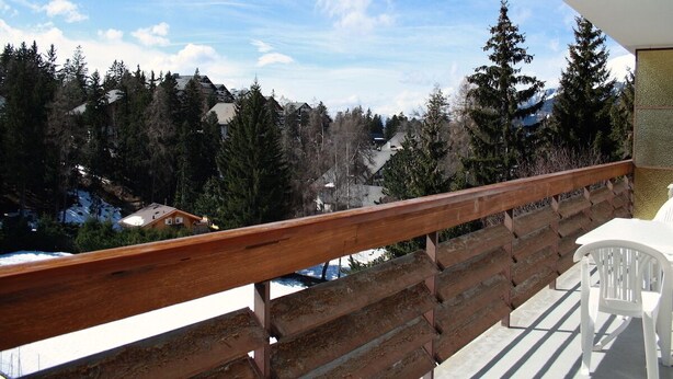 A balcony with a wooden railing overlooking a snowy landscape with houses and trees. - Cozy & Central - Palma B (Lens)