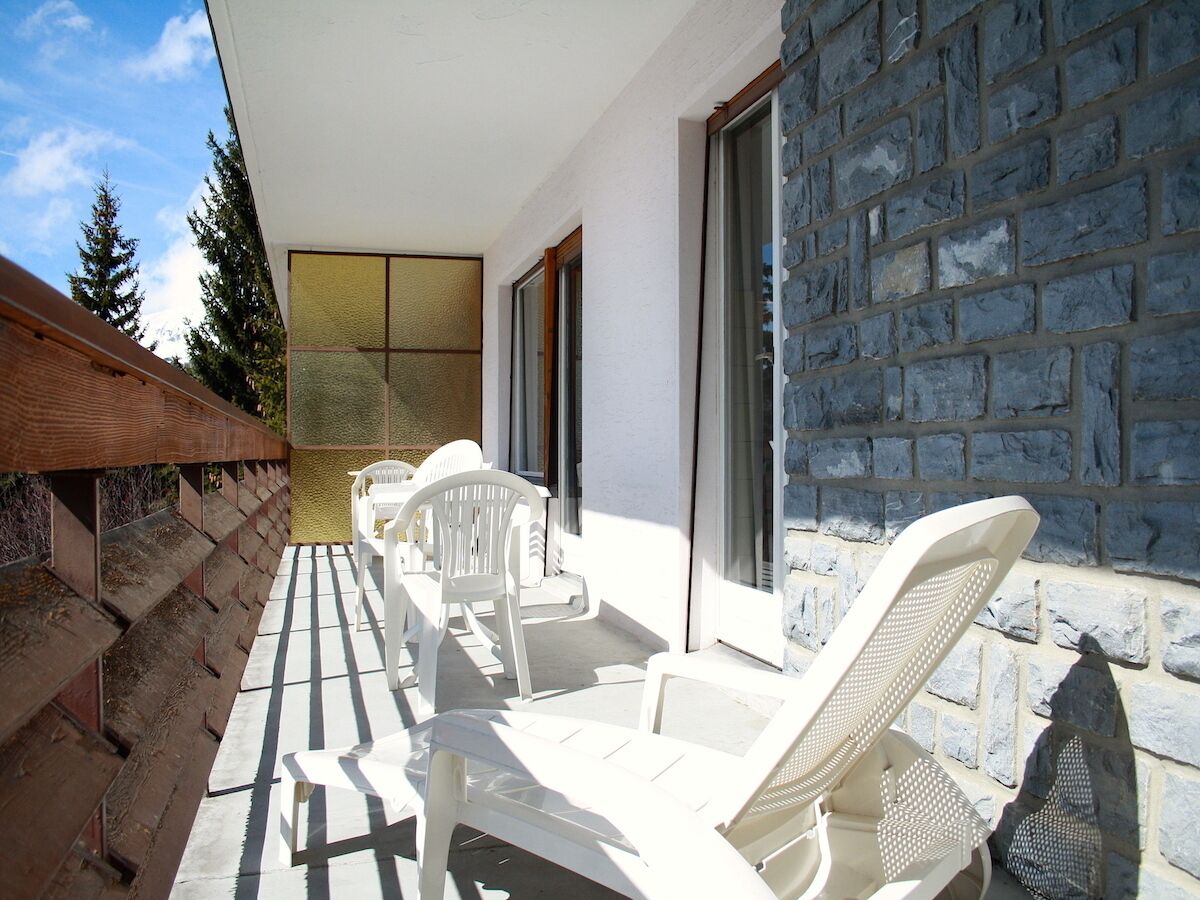 Uma varanda com cadeiras e mesa de plástico branco, uma parede de pedra e uma cerca de madeira.