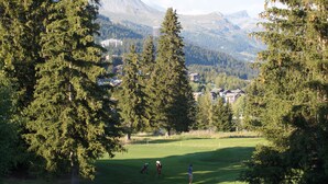 A golf course with a mountainous backdrop, surrounded by dense forests. - Charming & Intimate - Estoril (Crans-Montana)