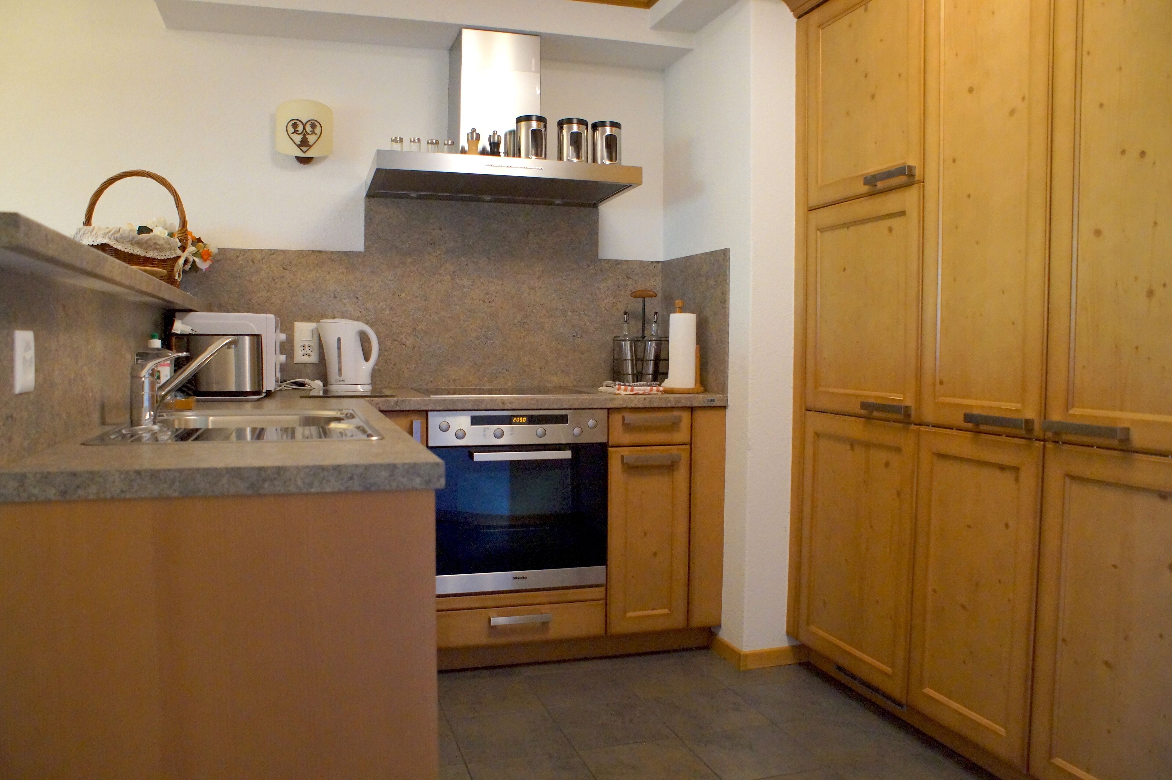 A compact kitchen with wooden cabinets, a built-in oven, a coffee maker, and a kettle.