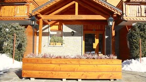A wooden building with a covered porch, a stone wall, and a sign that reads "ESTORIL". - Charming & Intimate - Estoril (Crans-Montana)