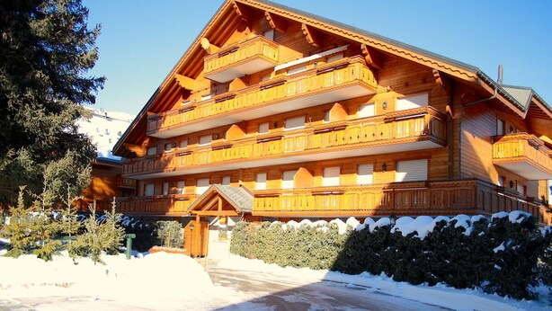 A large wooden chalet with multiple balconies and a snow-covered driveway. - Charming & Intimate - Estoril (Crans-Montana)