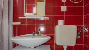 A bathroom with red tiled walls, a white sink, a toilet, a cabinet, and a window with a towel hanging on the door. - Vacation apartment GABI, Near the beach (Premantura)