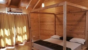 A wooden four-poster bed with a white mattress and dark bedding, a wooden floor, and a window with curtains. - I-Camp Resort (Wai)