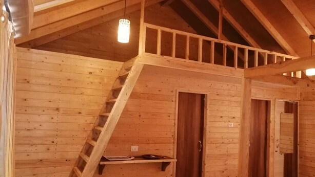 A wooden interior with a staircase leading to a loft area, wooden doors, and a metal railing. - I-Camp Resort (Wai)