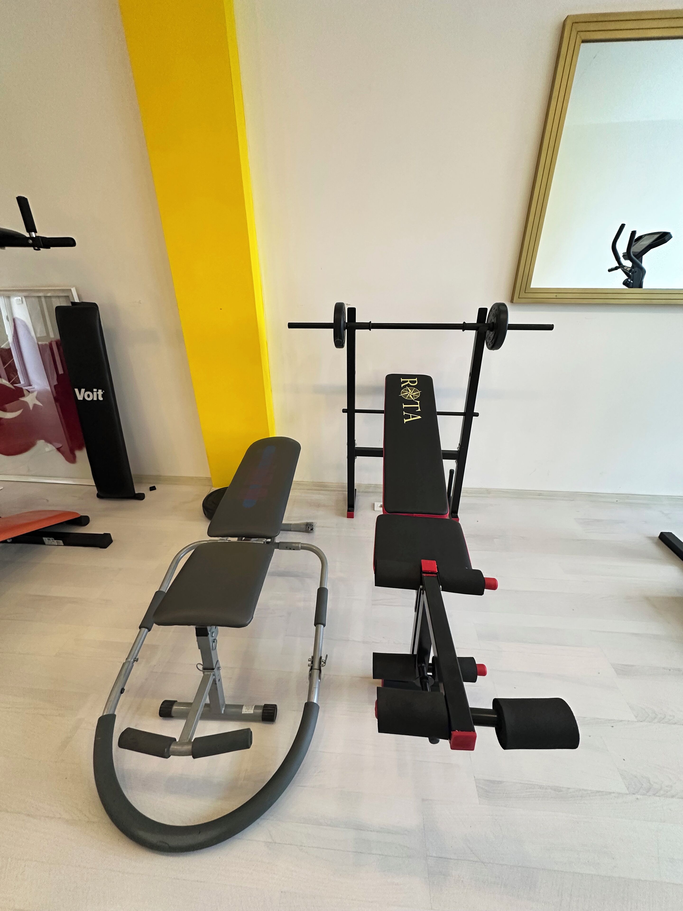 A gym with exercise equipment including a bench, a rowing machine, and a barbell.