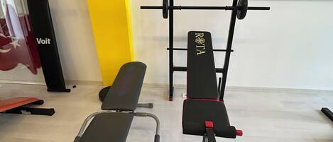 A gym with exercise equipment including a bench, a rowing machine, and a barbell.