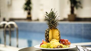 Una mesa de comedor con un plato de fruta que incluye piña, uvas y trozos de mango.