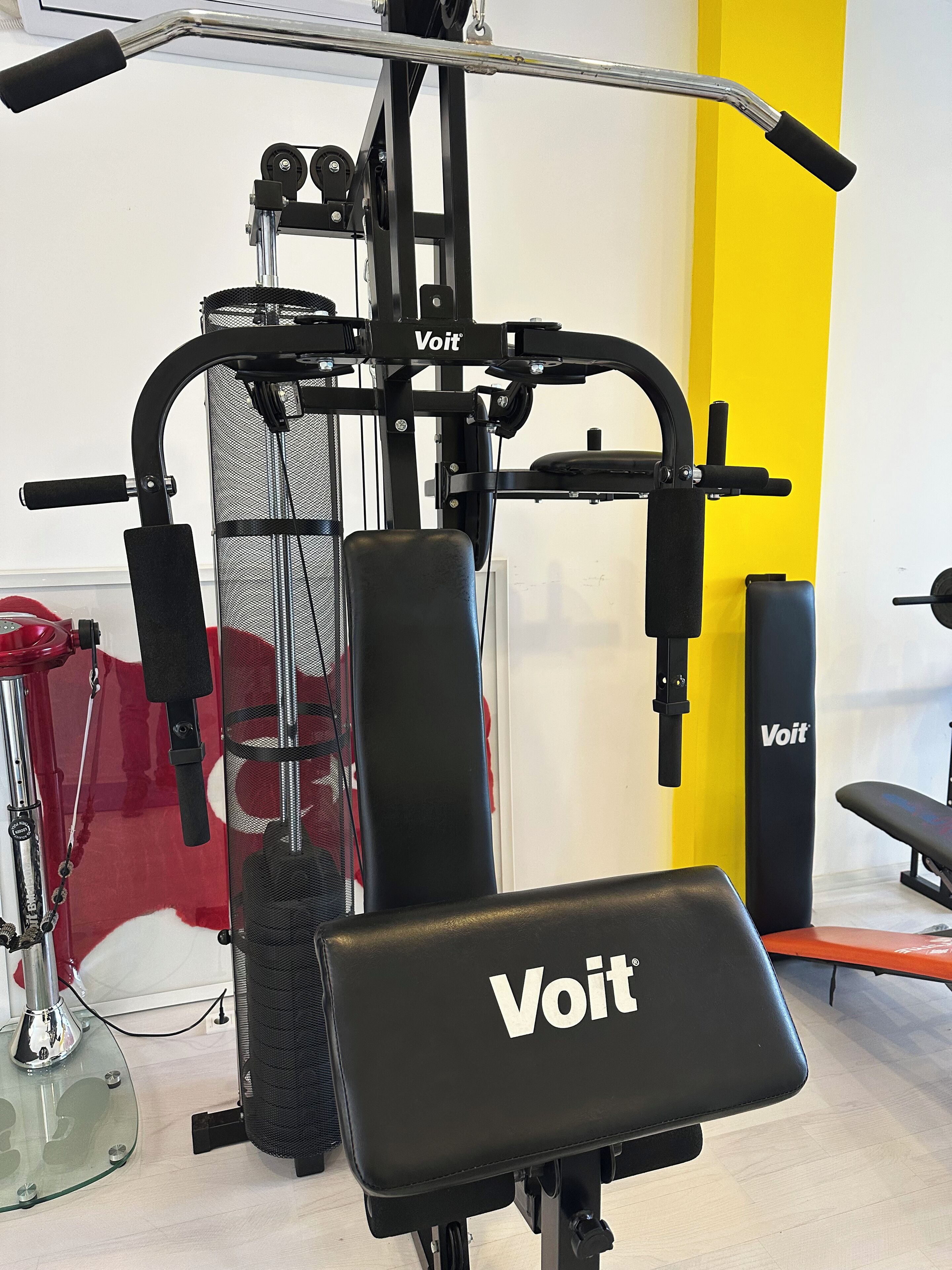 A gym with a black and red exercise machine, a black weight bench, and a yellow wall.