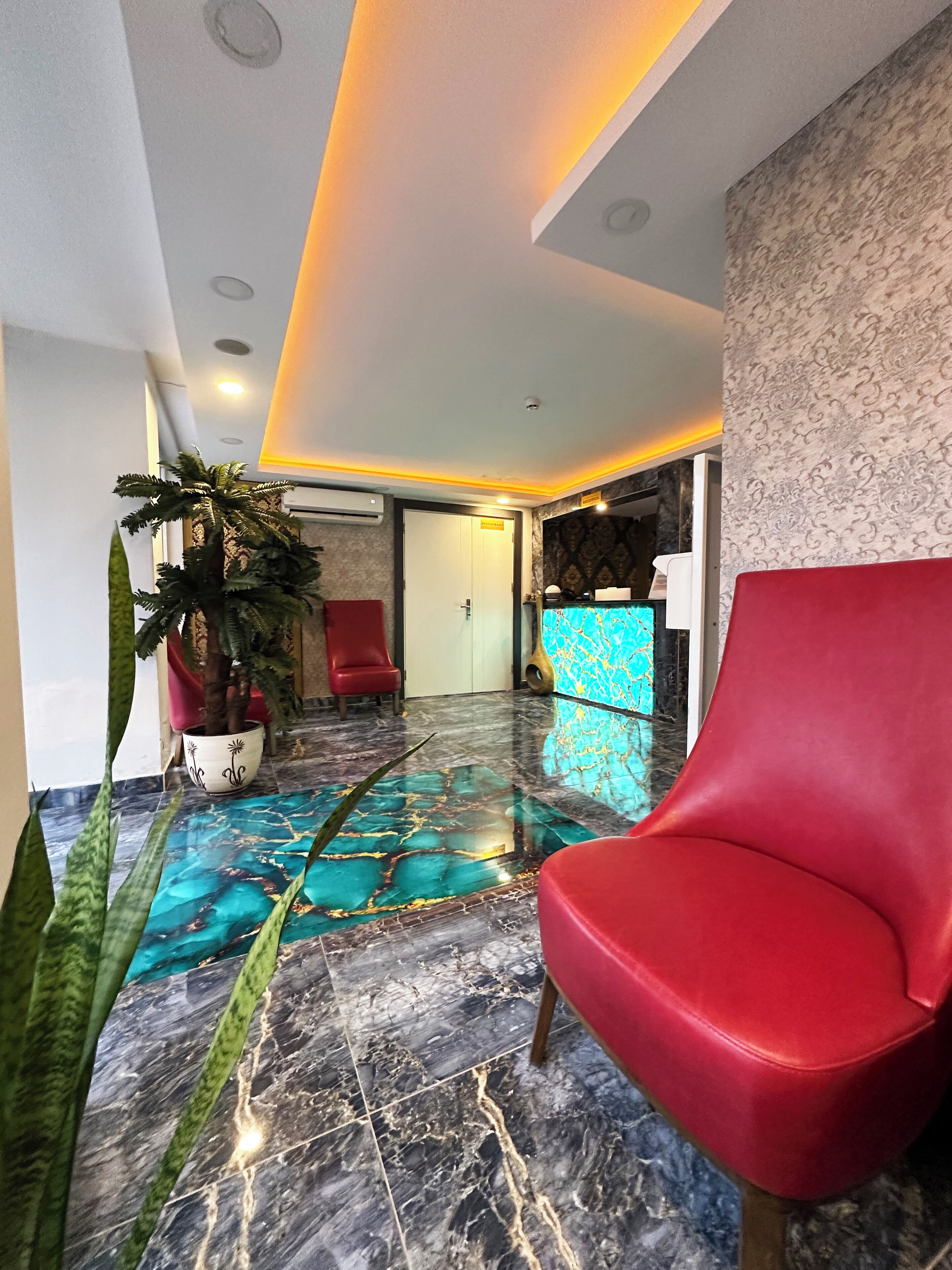 A hotel lobby with a marble floor, a red chair, a potted plant, and a reception desk.