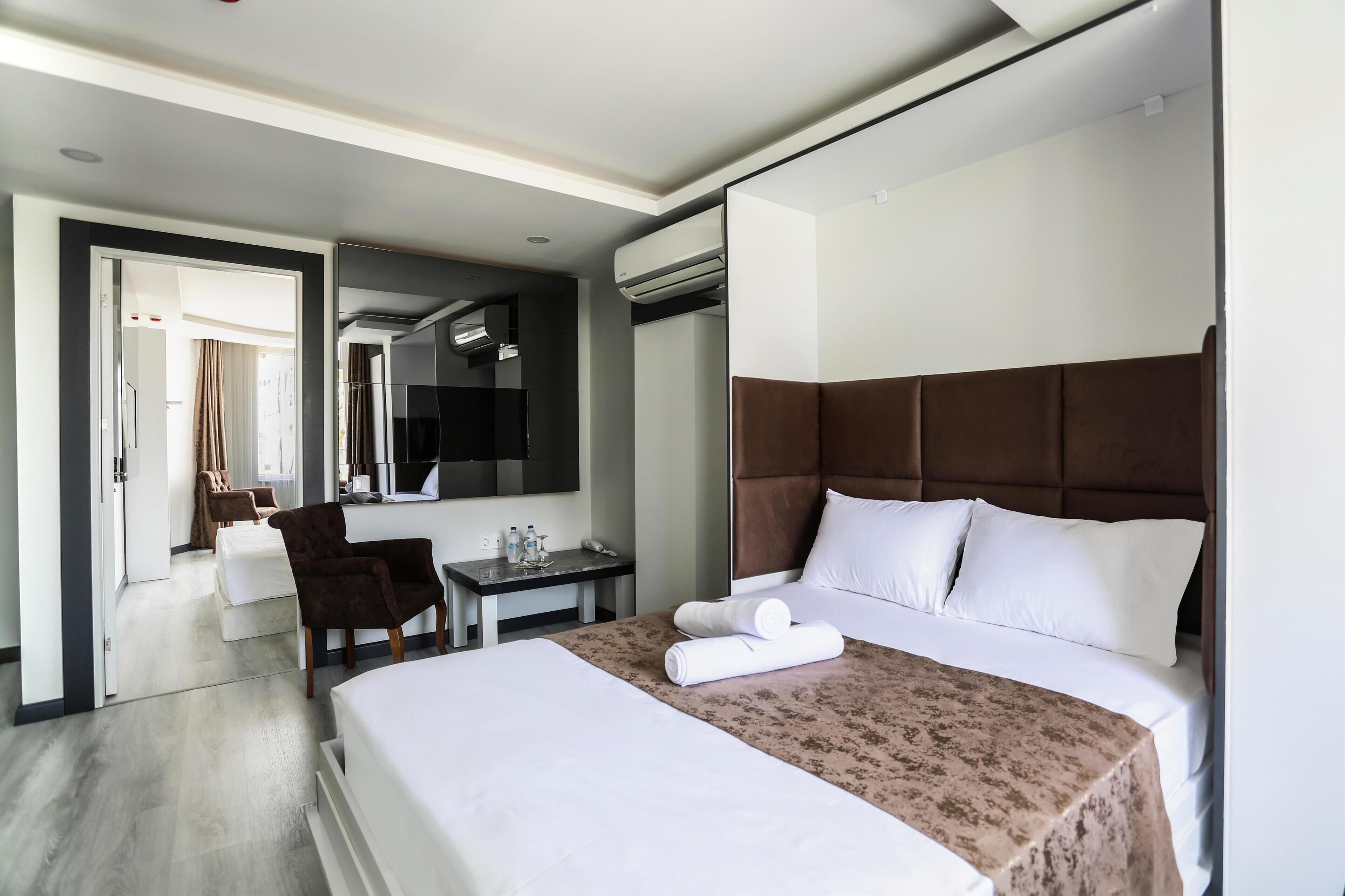 A hotel room with a large bed, a desk, a chair, a mirror, and an air conditioning unit.