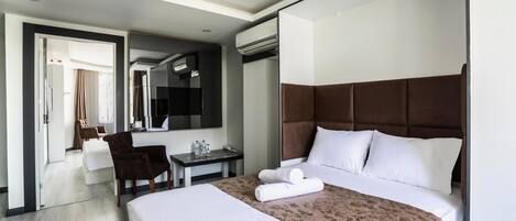 A hotel room with a large bed, a desk, a chair, a mirror, and an air conditioning unit.