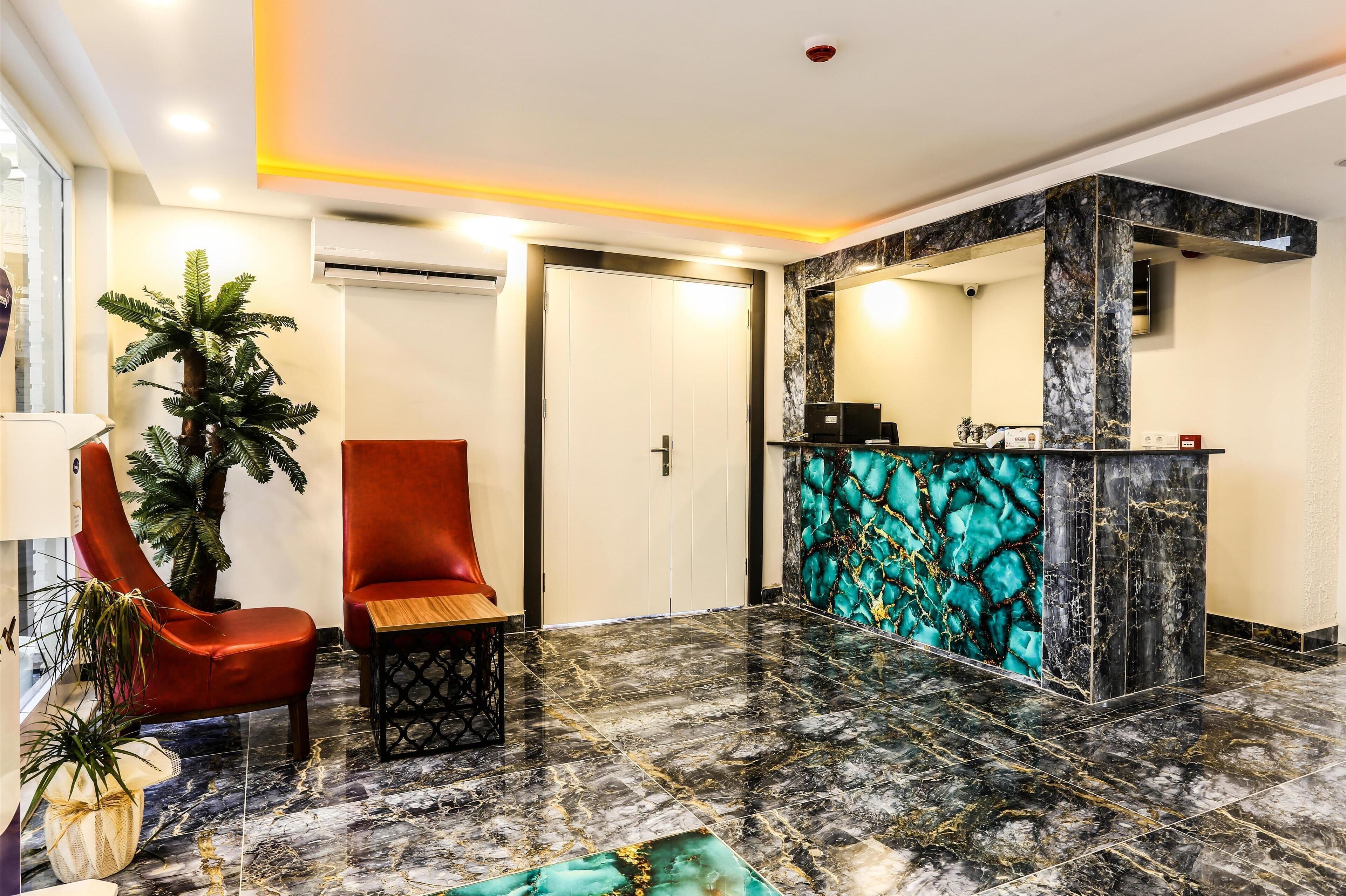 A lobby with a reception desk, a red chair, a wooden table, and a potted plant.