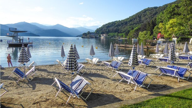 A beach with sun loungers and umbrellas, a lifeguard tower, and mountains in the background. - Nice home in Gozzano with WiFi (Gozzano)