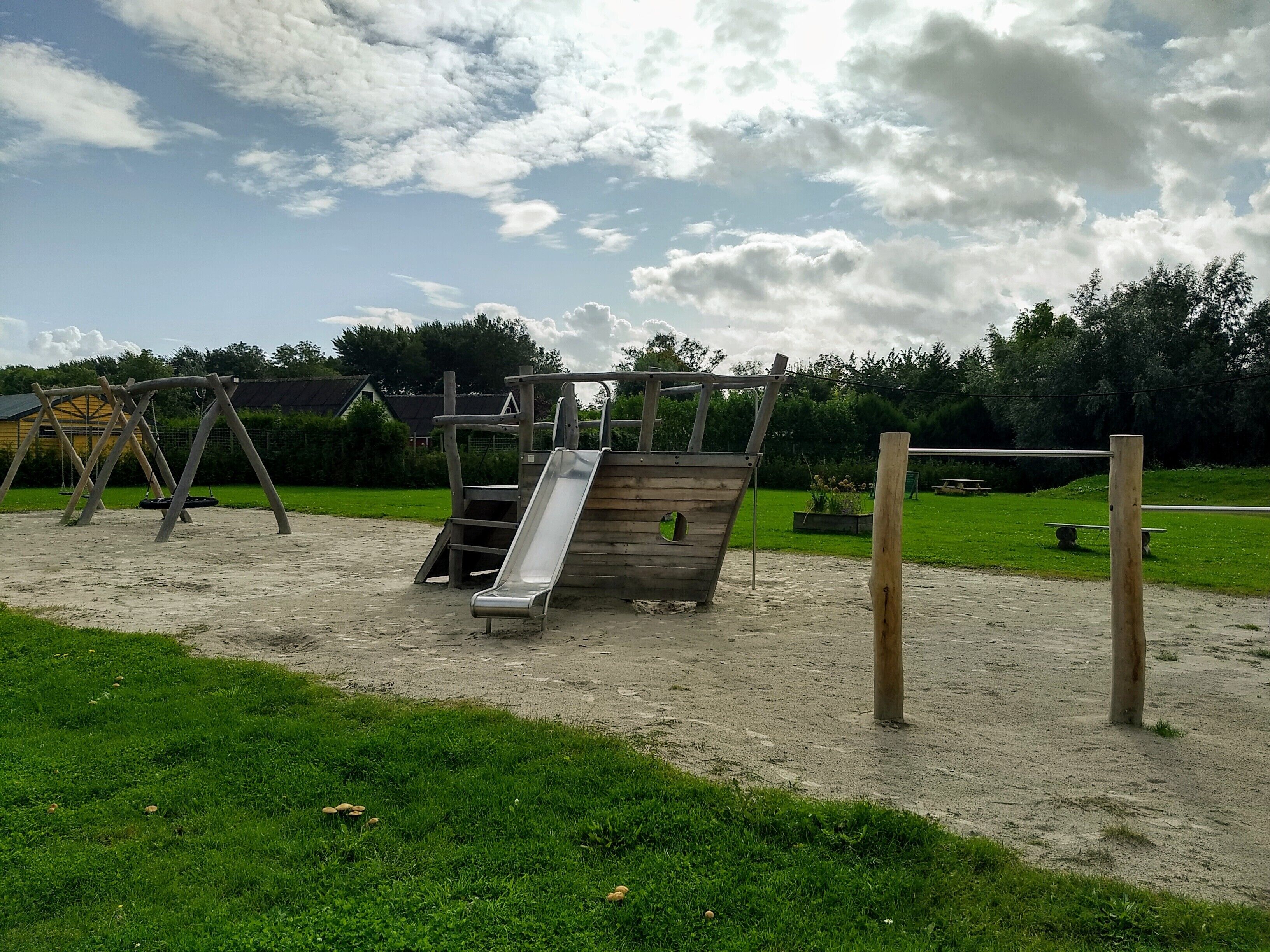 Een speeltuin met schommels, een glijbaan en zand.