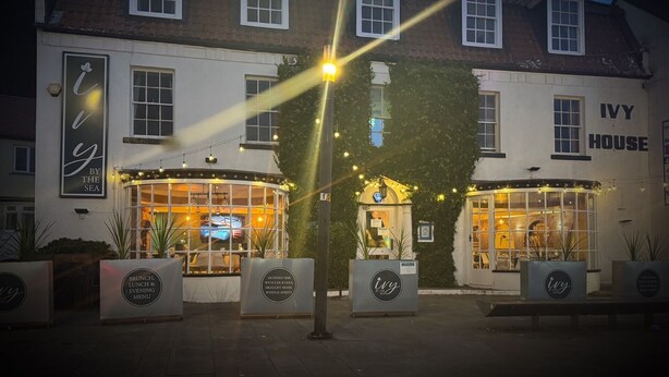 A building with a sign reading "Ivy House" and a sign for "Ivy by the Sea" with outdoor seating and string lights. - Ivy By The Sea (Scarborough)