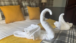 A bed with a plaid bedspread, two gold pillows, and two white swan-shaped towels. - Ivy By The Sea (Scarborough)