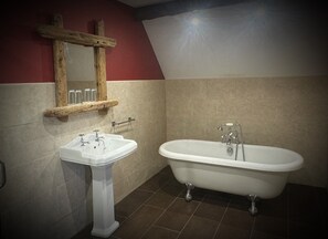 Ein Badezimmer mit freistehender Badewanne, einem Standwaschbecken und einem spiegel mit Holzrahmen.