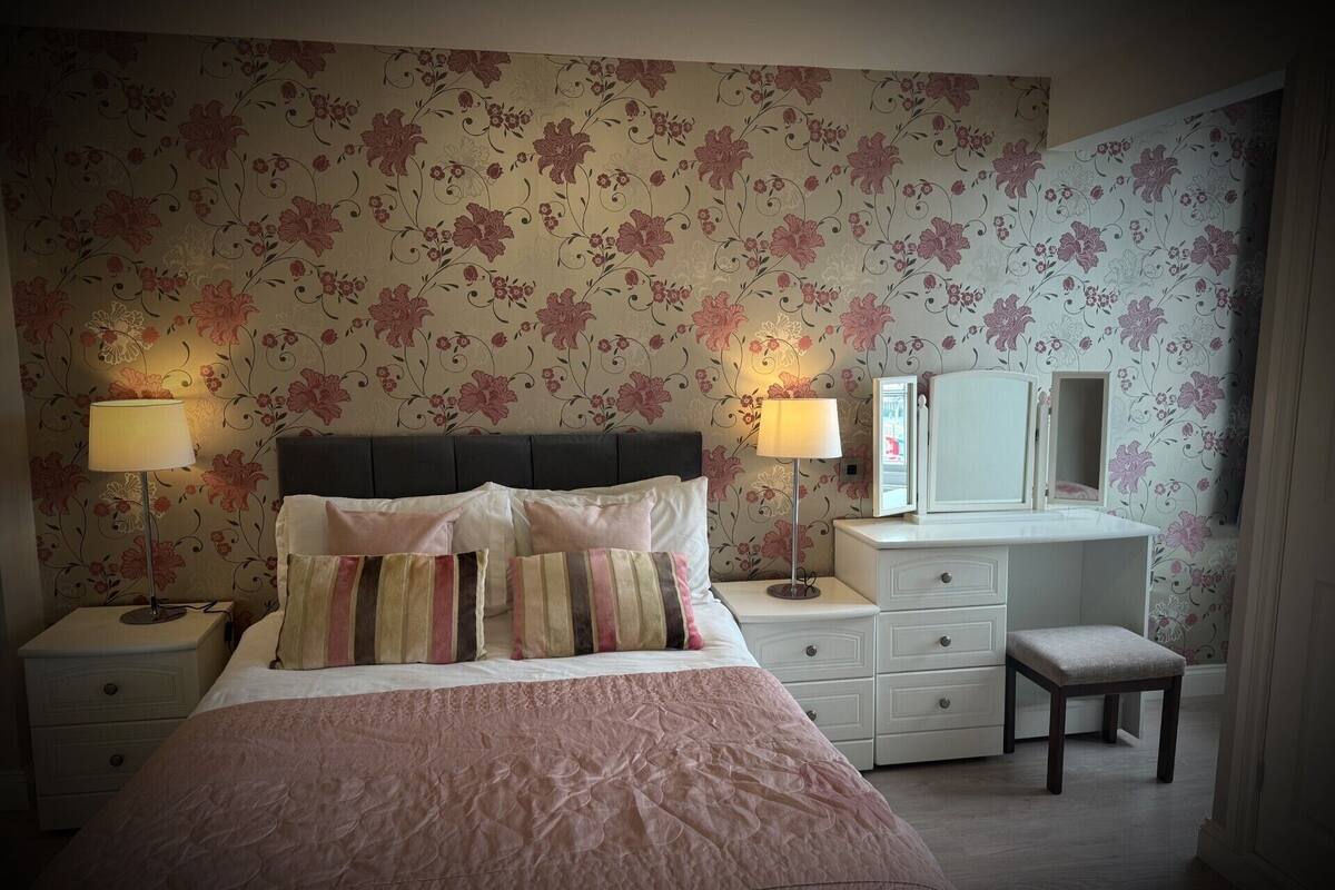 A bedroom with a bed, two bedside tables with lamps, a dresser, a mirror, and a bench.