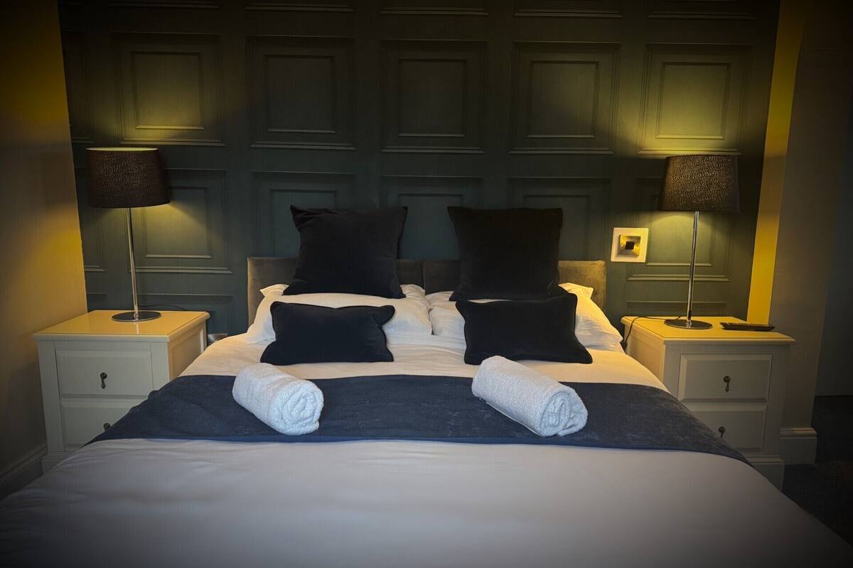 A neatly made bed with two pillows, two rolled towels, and two bedside tables with lamps.
