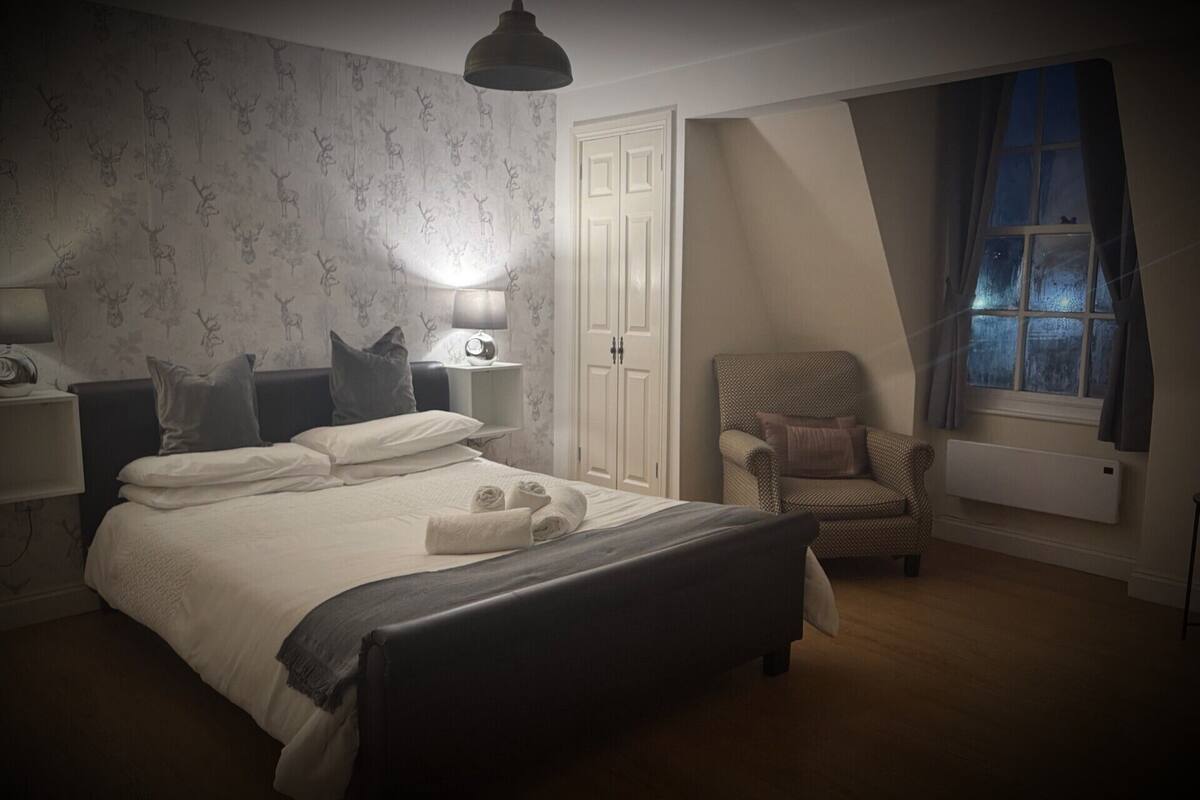 A bedroom with a bed, bedside lamps, a chair, a window, and a radiator.