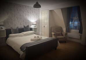 Ein Schlafzimmer mit einem Bett, Nachttischlampen, einem Sessel, einem Fenster und einer Heizung.