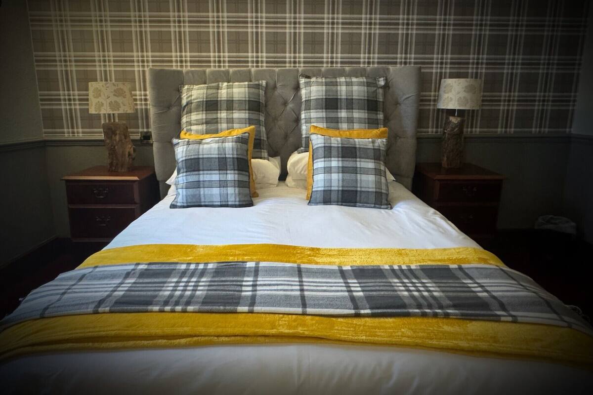 A neatly made bed with a plaid bedspread and pillows, flanked by two bedside tables with lamps.