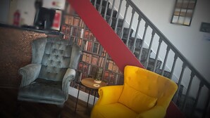 A staircase with a red handrail, a grey armchair, and a yellow armchair in a room with a bookshelf in the background. - Ivy By The Sea (Scarborough)