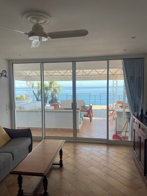 Una stanza con una porta a vetri scorrevoli che dà su un balcone con vista sull'oceano.