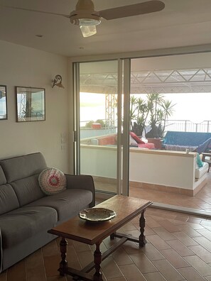 Un salon avec un canapé, une table et une vue sur un balcon agrémenté de plantes et doté d’une balustrade.