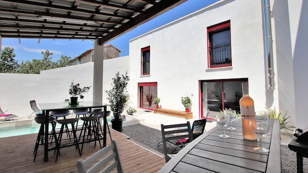 Eine überdachte Terrasse im Freien mit Pool, Tisch mit Stühlen und Topfpflanzen.