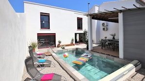 Ein moderner Poolbereich im Freien mit Glasveranda, Liegestühlen und Esstisch.