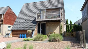 A two-story building with a sloped roof, a wooden deck, and a small garden area with shrubs and a tree. - Amazing home in Grou with WiFi (Grou)