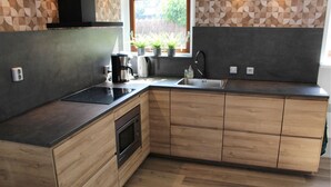 A modern kitchen with a built-in stove, oven, and sink. There are wooden cabinets and a window with a view of greenery outside. - Amazing home in Grou with WiFi (Grou)